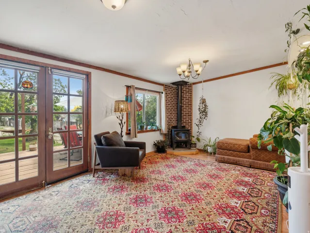 Wood-finish flooring, brick-backed wood-burning stove, multiple windows, double glass-paneled patio doors, and a ceiling-mounted chandelier