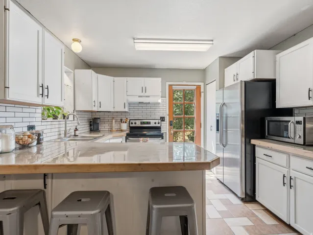 White cabinetry with black hardware, subway tile backsplash, stainless steel appliances, and a wood-finish countertop