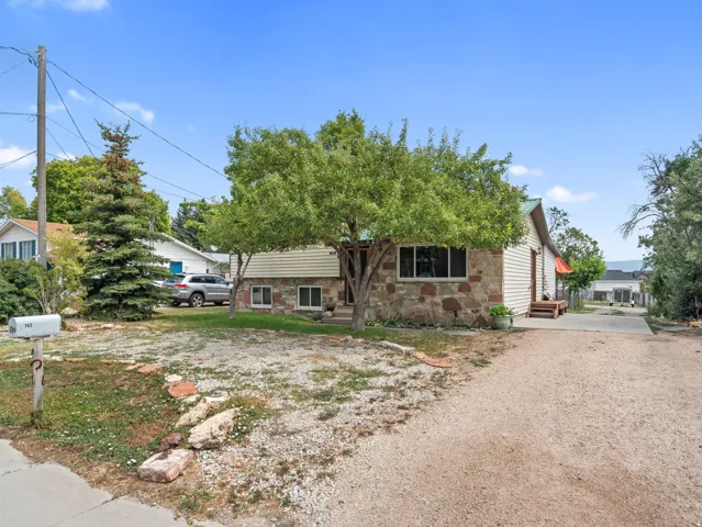 Stone and siding exterior with mature trees and a gravel driveway