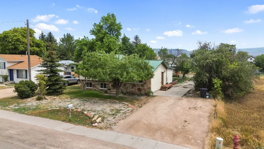 Stone exterior accents, mature trees, green metal roof, light-colored siding, and a spacious gravel driveway