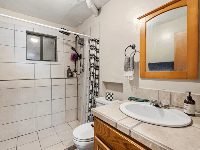 Tiled shower surround with an integrated window, wood-finish vanity with tiled countertop, and a wall-mounted mirror