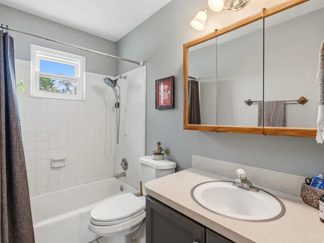 Full bathtub with white tile surround, white vanity with integrated sink, wood-framed medicine cabinet with triple mirrors, and an overhead light fixture