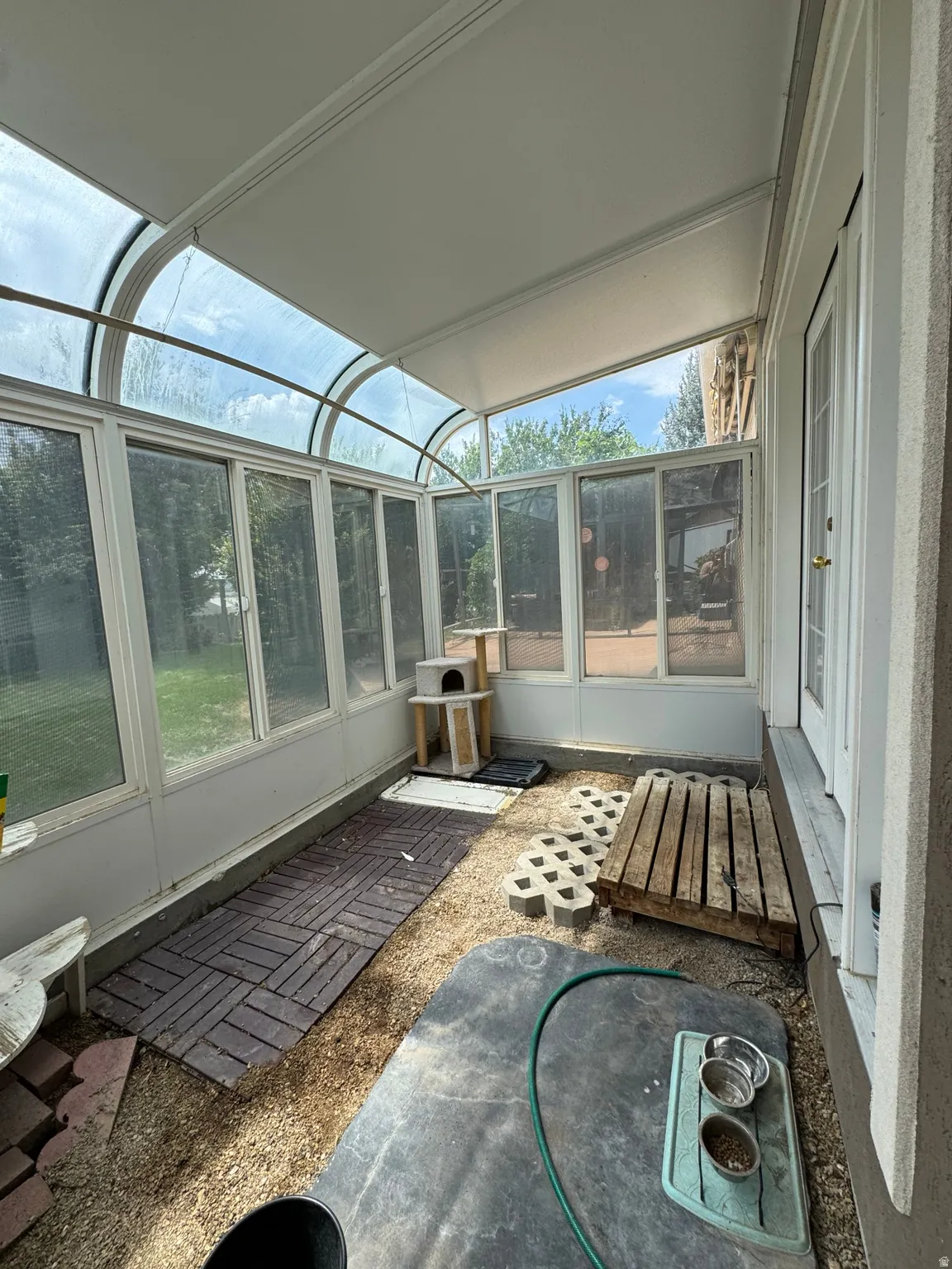 Enclosed sunroom featuring a clear arched roof, full-height windows, a white paneled ceiling, and a white exterior door