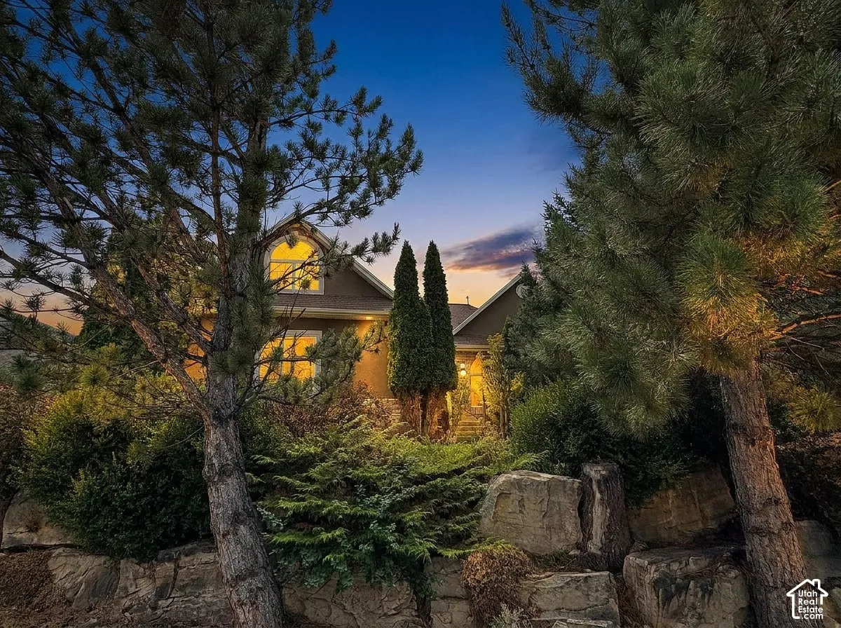 Front exterior featuring a dormer window, established landscaping, and natural rock retaining walls