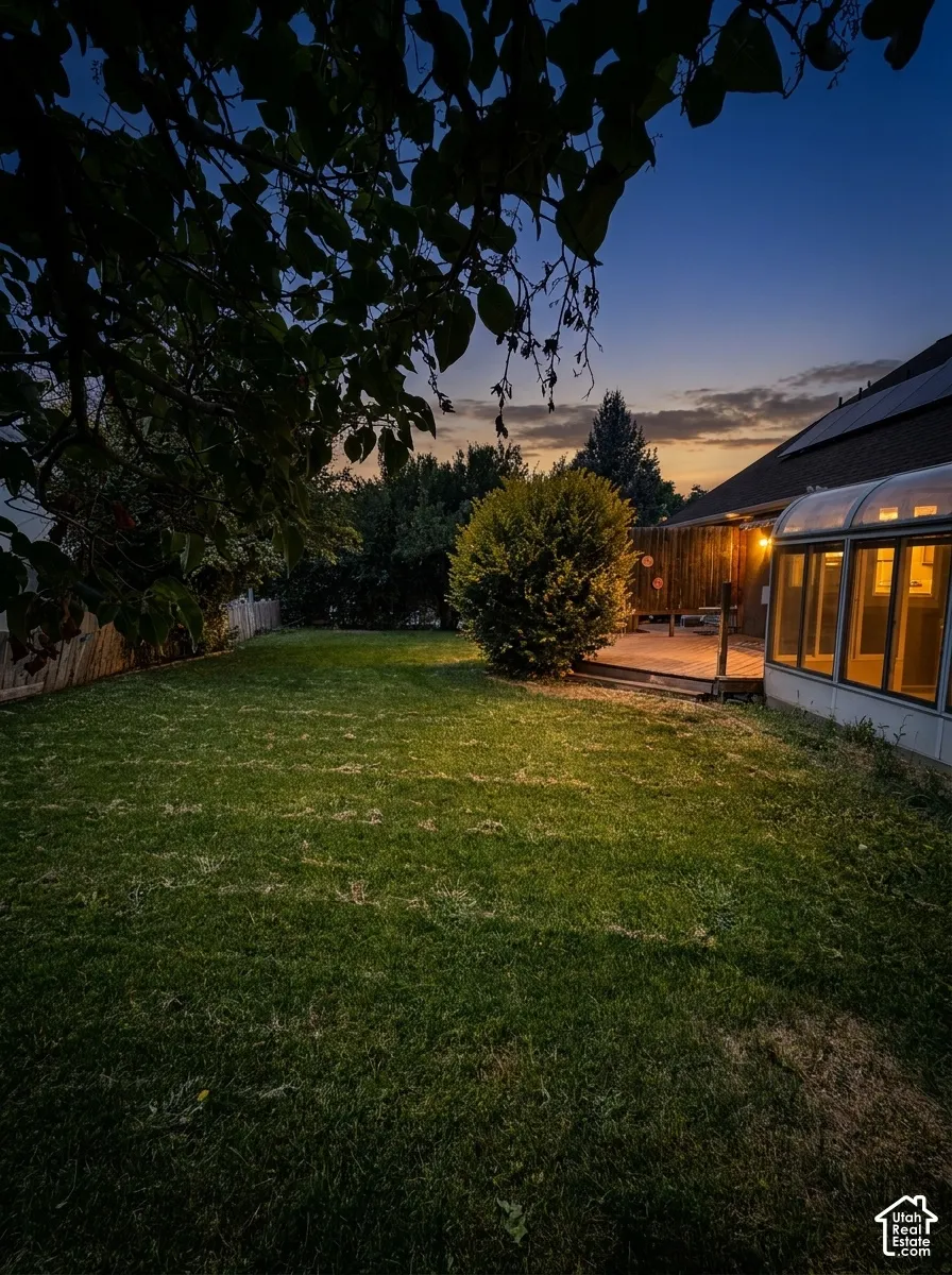 Expansive backyard featuring a manicured lawn, a wooden fence, a rear deck, and a sunroom with an arched roof