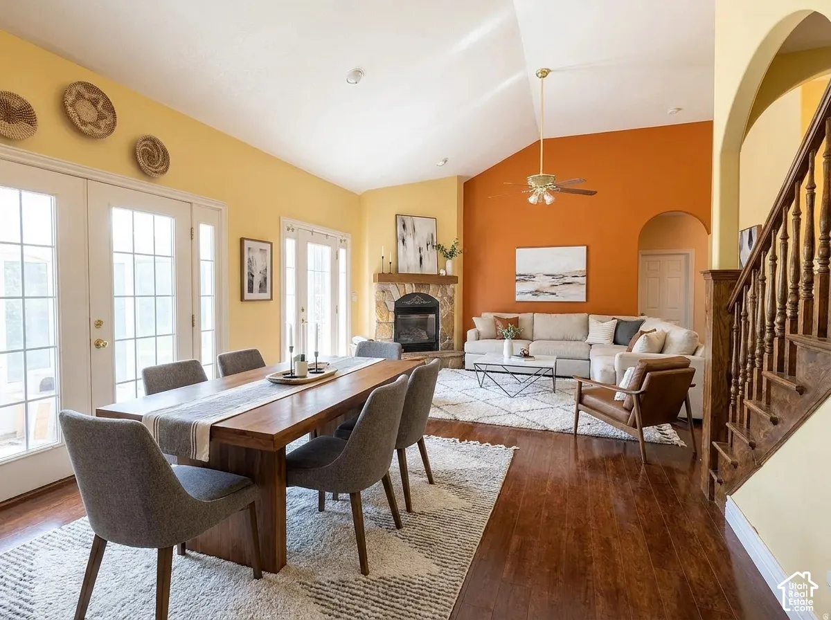 Vaulted ceiling with an overhead fan, stone fireplace, wood-finish flooring, and multiple sets of French doors