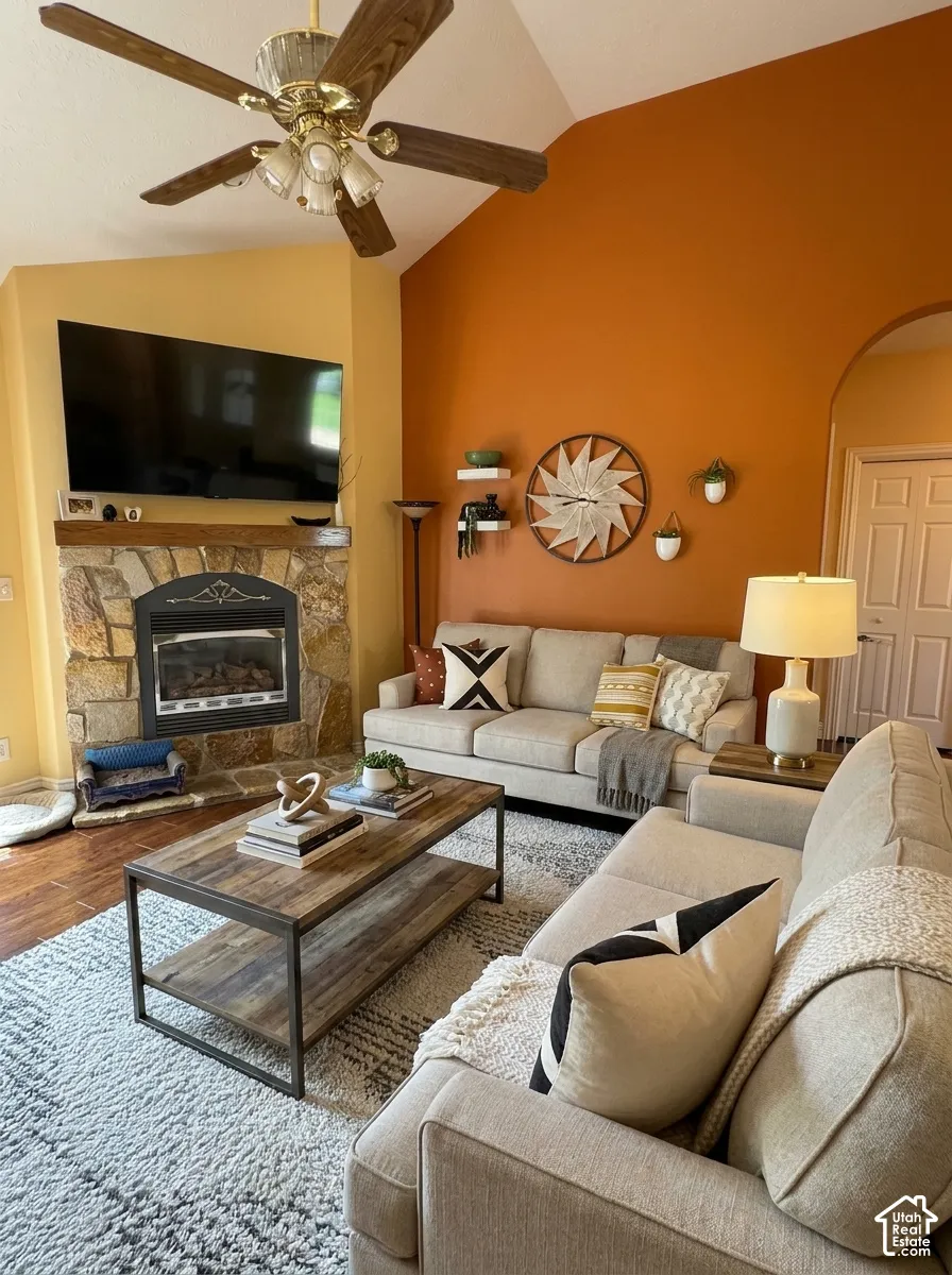 Vaulted ceiling with a wood-finish ceiling fan, stone-clad fireplace, and wood-finish flooring