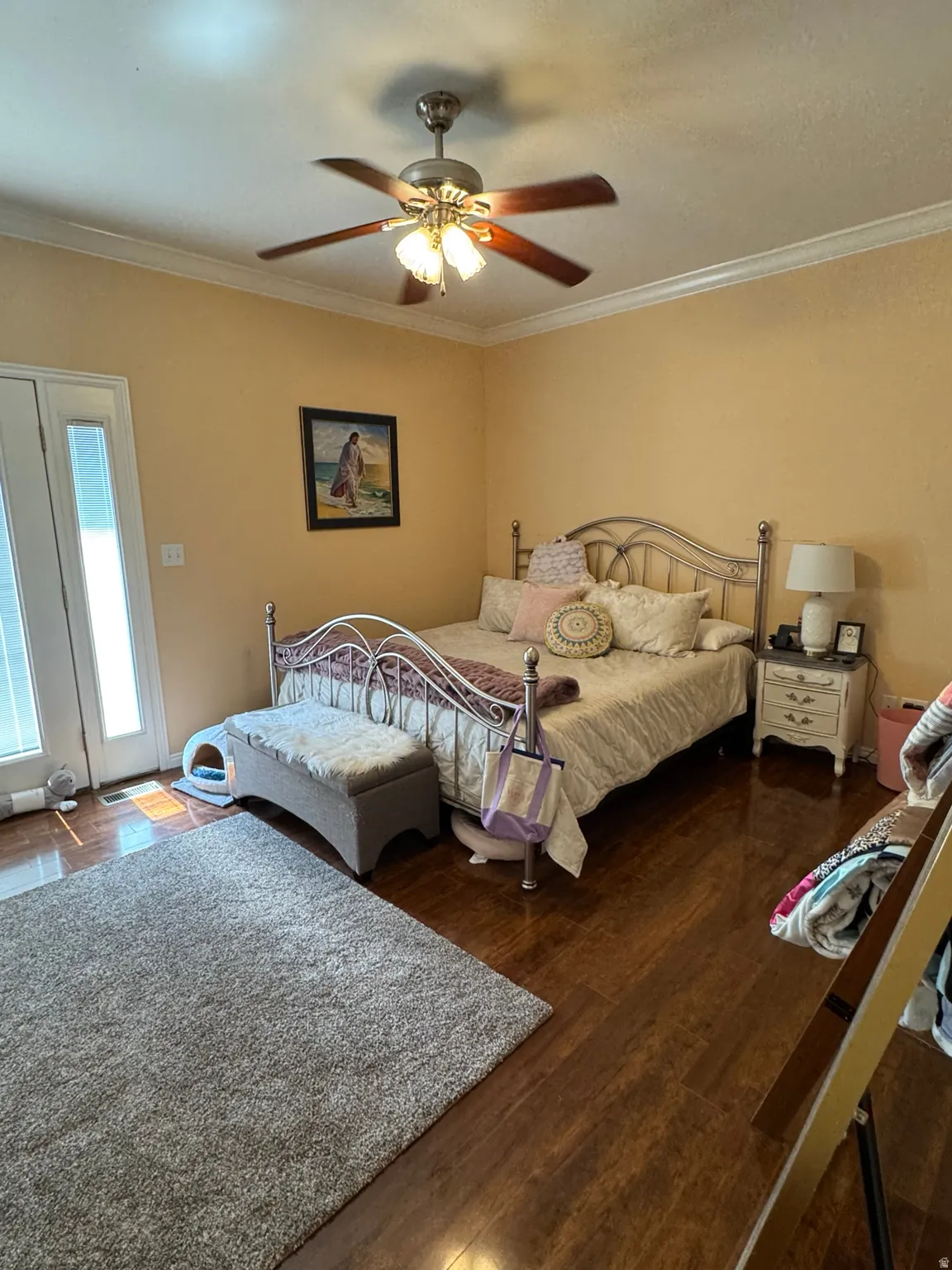 Primary suite, attached bathroom, Wood-finish flooring, crown molding, double doors with integrated windowpanes, and a ceiling fan with integrated lighting