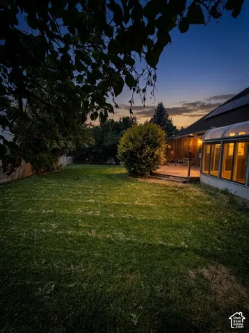Expansive backyard featuring a manicured lawn, a wooden fence, a rear deck, and a sunroom with an arched roof