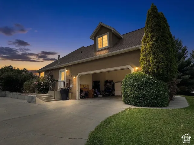 Stucco exterior with dormer window, attached garage, concrete driveway, and established landscaping