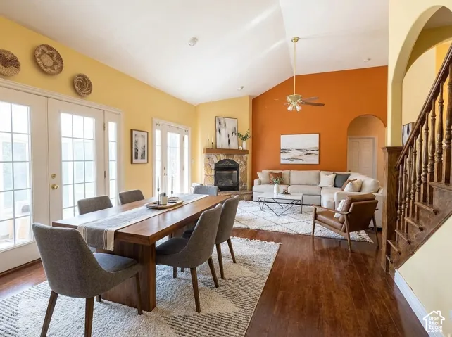 Vaulted ceiling with an overhead fan, stone fireplace, wood-finish flooring, and multiple sets of French doors