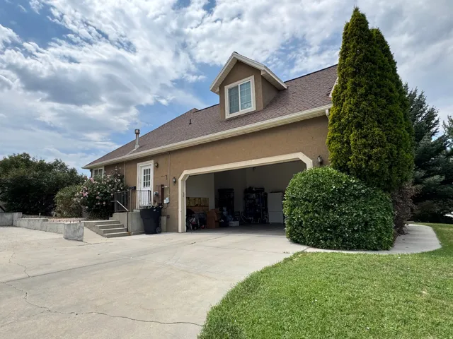 Two-car garage with concrete driveway, dormer window, and mature landscaping