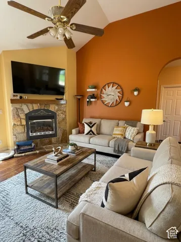 Vaulted ceiling with a wood-finish ceiling fan, stone-clad fireplace, and wood-finish flooring