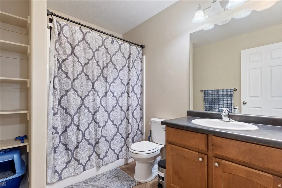 Built-in shelving, wood-finish vanity with cabinet storage, integrated vanity sink, countertop with a matte finish, and a shower with a curtain rod