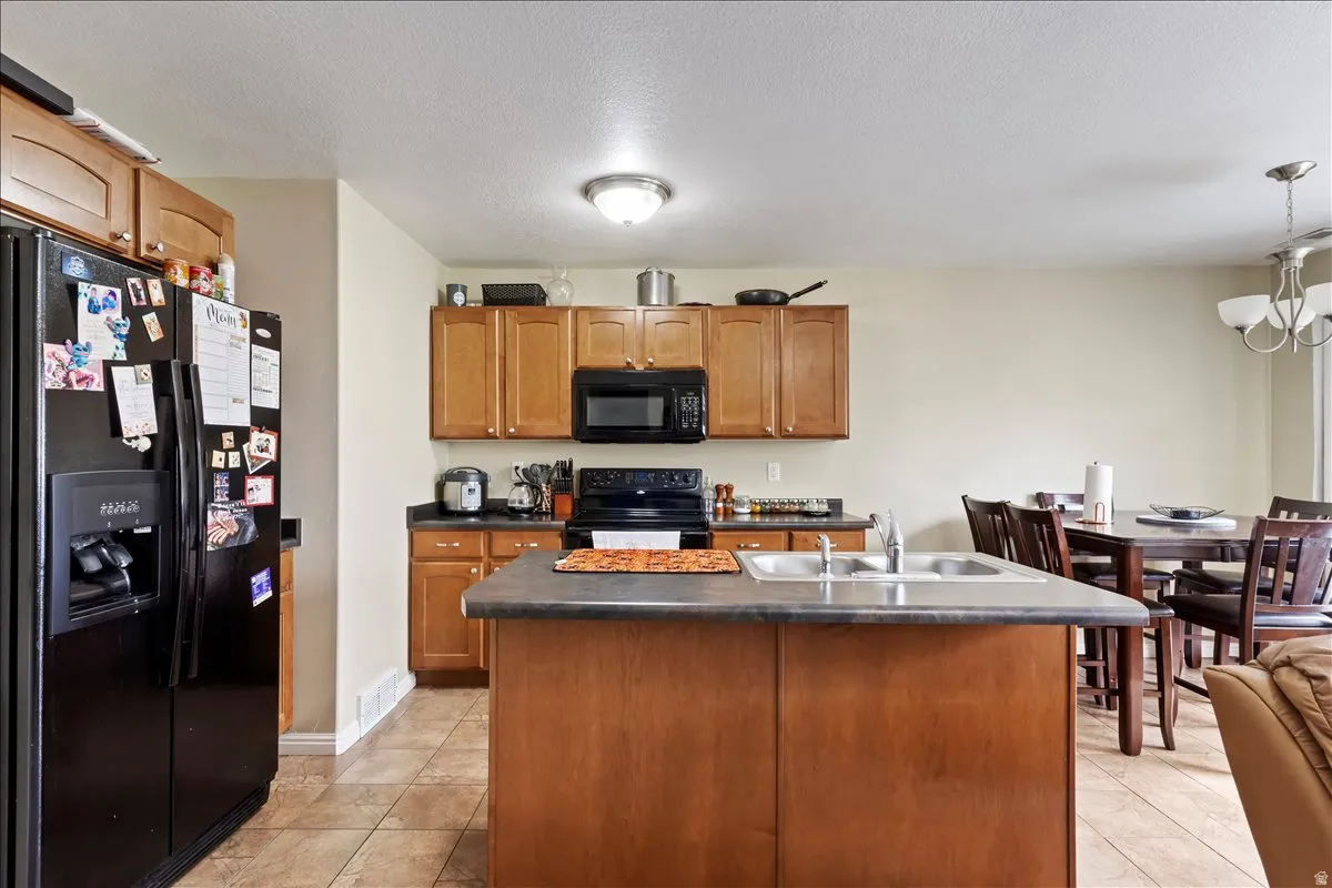 Kitchen featuring wood cabinetry, dark countertops, a double basin sink, and tile flooring