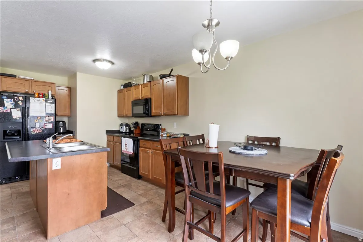 Kitchen featuring wood-finish cabinetry, black appliances, a kitchen island with a sink, and tile flooring