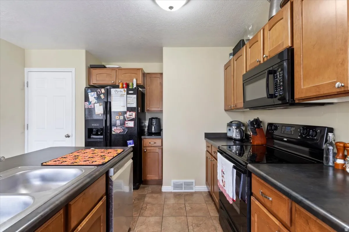 Kitchen featuring wood-finish cabinetry, black appliances, a double basin sink, and tiled flooring