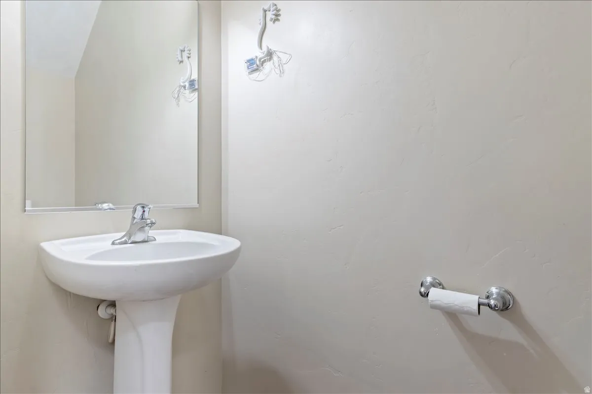 Pedestal sink with chrome faucet, clear wall-mounted mirror, and neutral wall finish