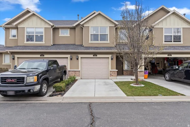 Stucco exterior with gabled roof lines, attached garages, concrete driveways, and manicured lawn