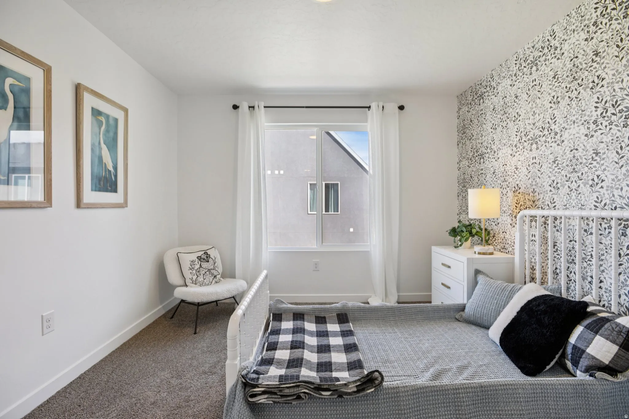 Wall-to-wall carpeting, window with roller shade, and an accent wall featuring patterned wallpaper