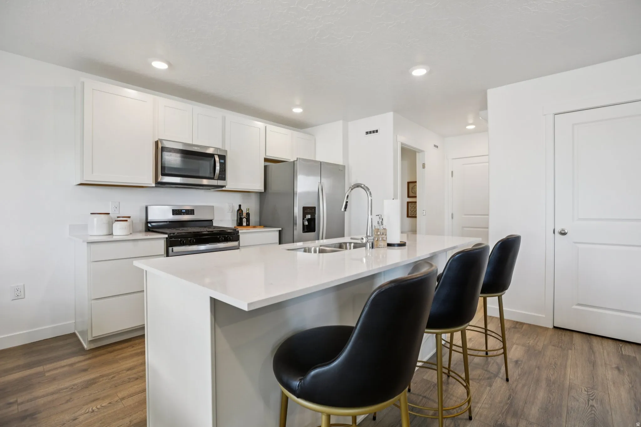 Kitchen featuring white cabinetry, stainless steel appliances, an island with seating, and wood-finish flooring