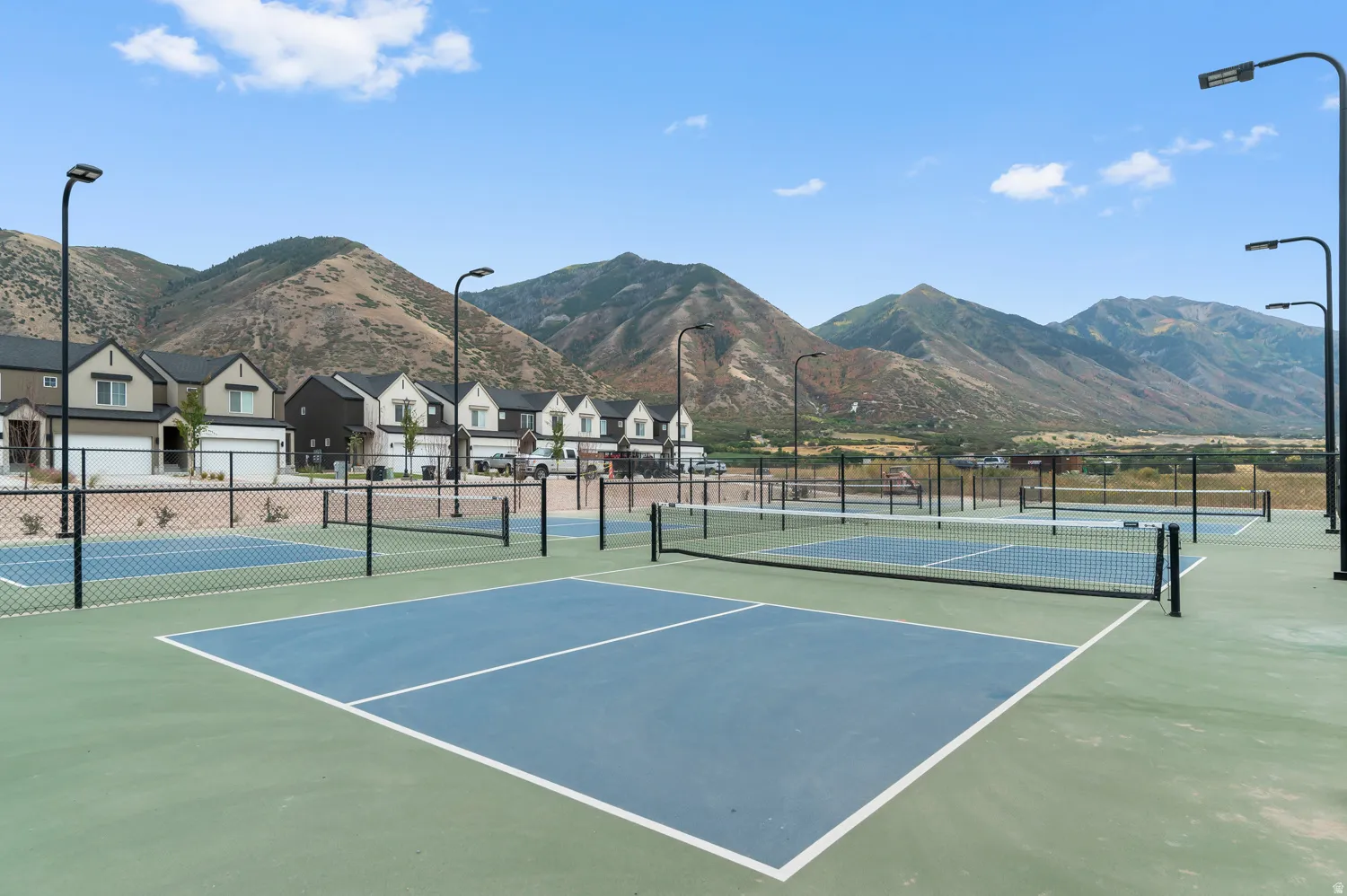 Multiple outdoor courts with blue and green surfaces, equipped with nets and perimeter fencing