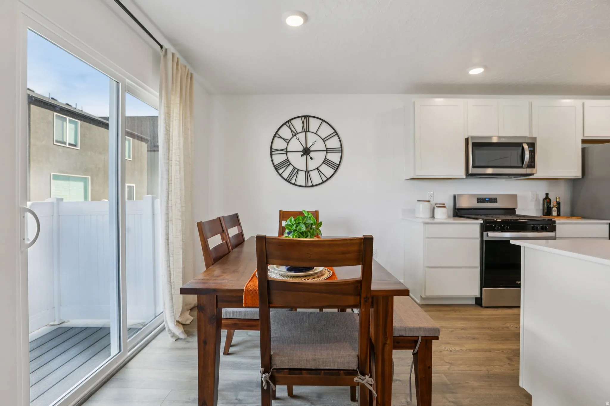 Wood-finish flooring throughout, white cabinetry, stainless steel appliances, and a sliding glass door to an exterior deck