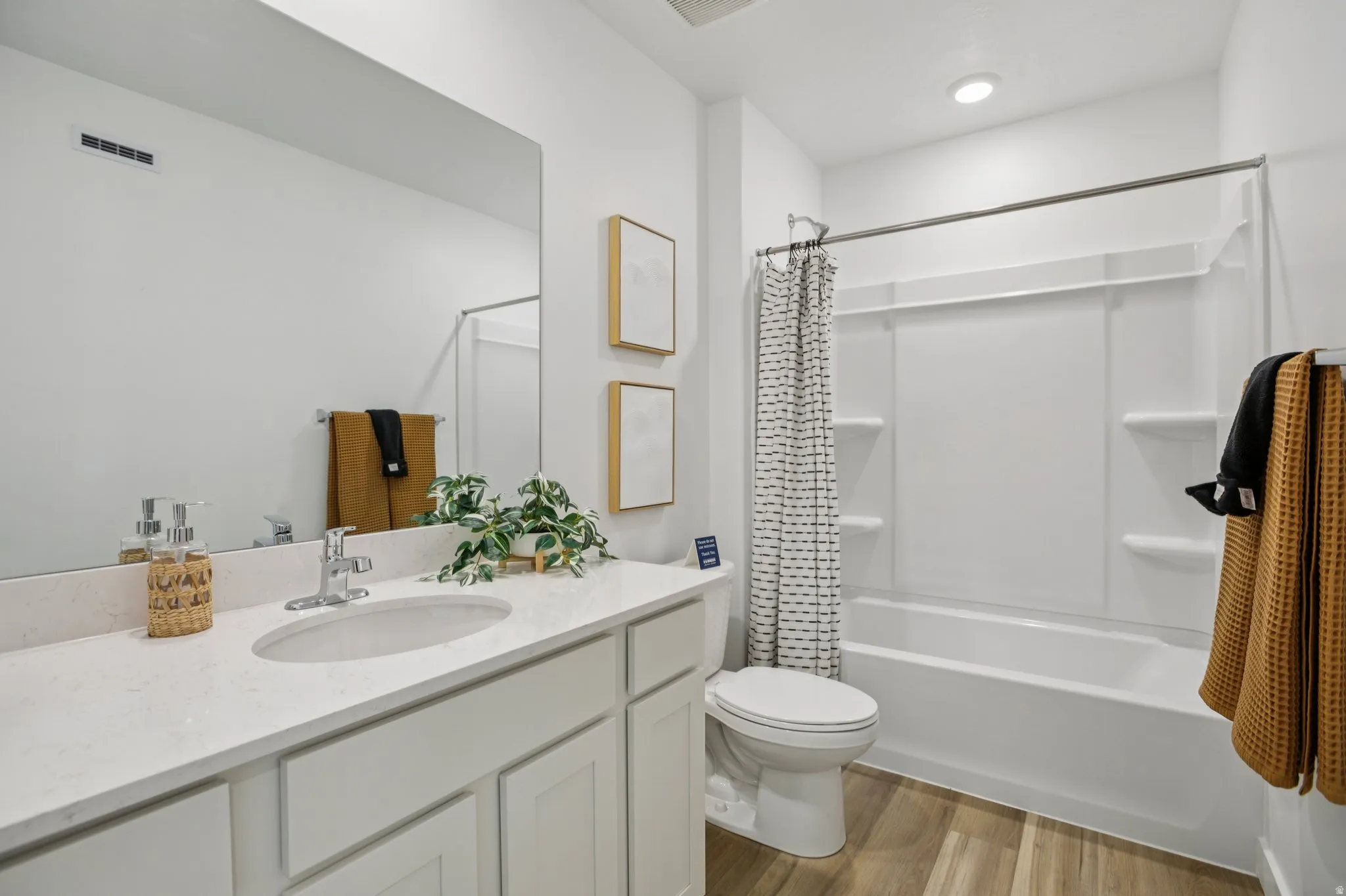 Bathroom featuring a single vanity with an undermount sink, a full-width mirror, a tub-shower combination, and wood-finish flooring