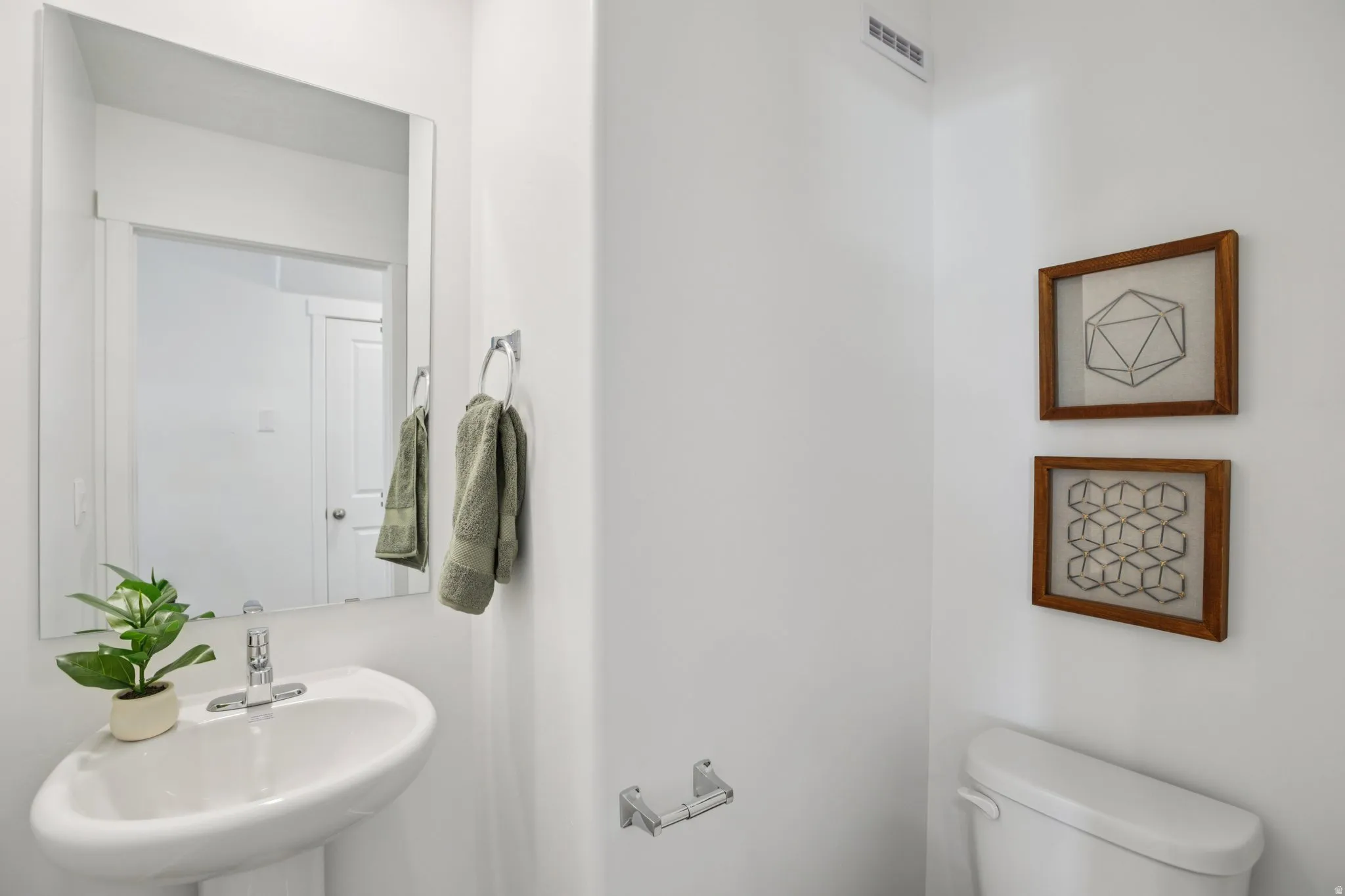 Pedestal sink with chrome faucet, wall-mounted mirror, and white toilet