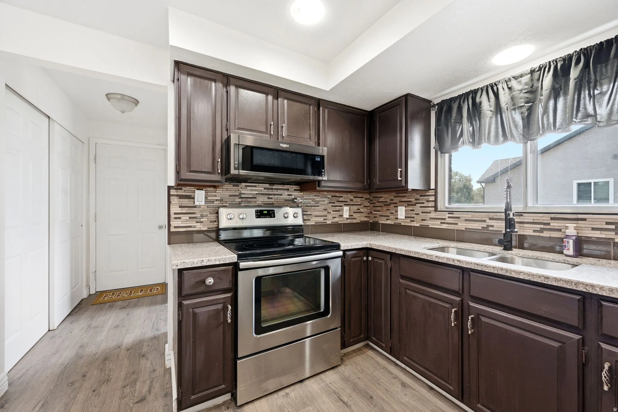 Kitchen featuring wood-finish cabinetry, stainless steel appliances, a multi-tone tile backsplash, and a double basin sink