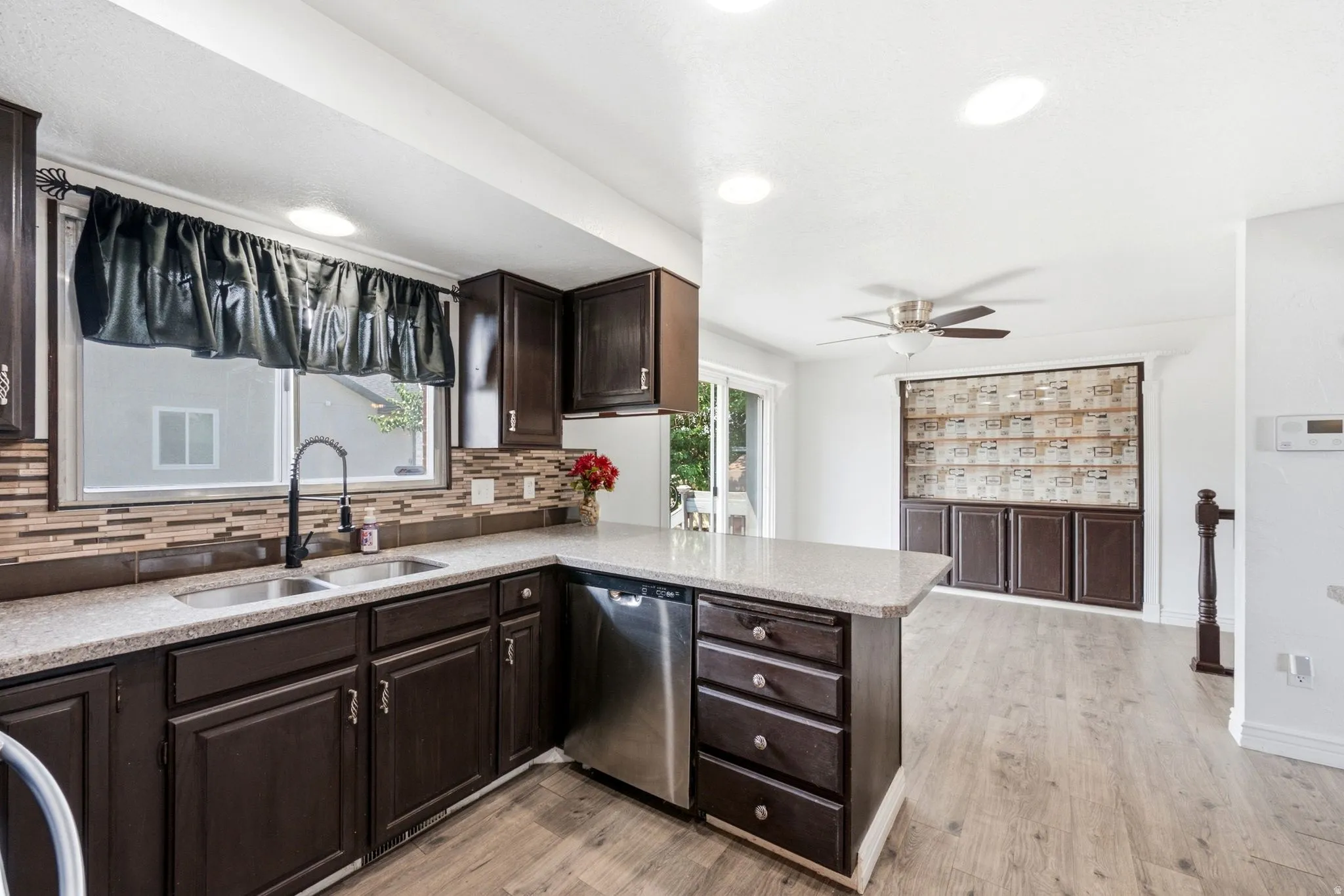 Kitchen featuring wood-finish cabinetry, light-colored countertops, stainless steel dishwasher, and a mosaic tile backsplash