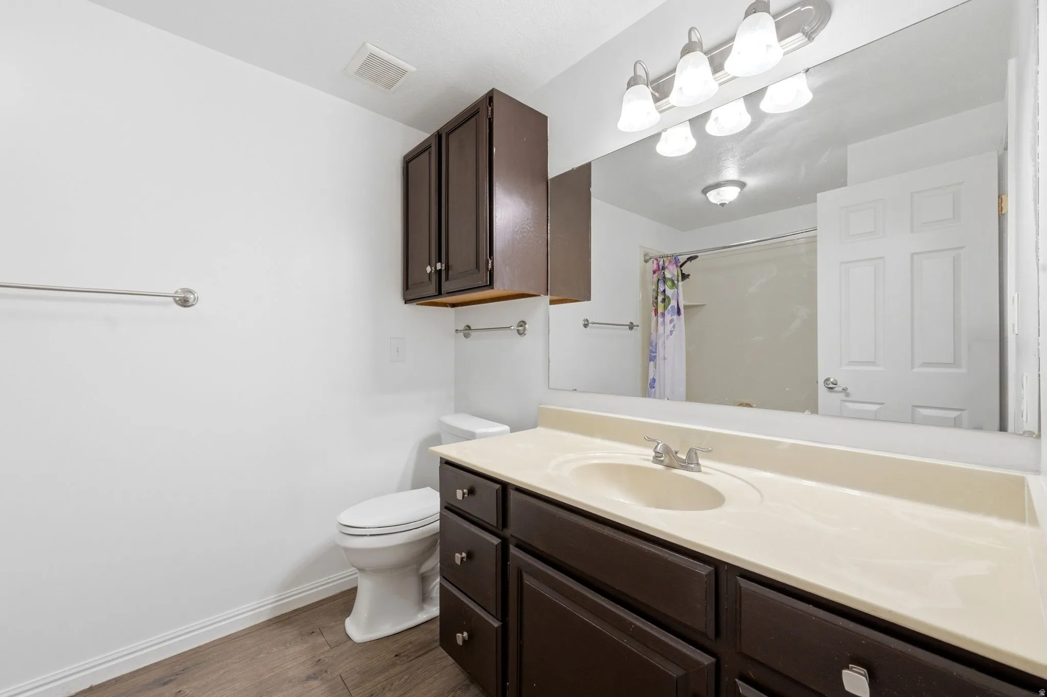 Wood-finish flooring, dark wood-finish vanity with ample storage, integrated sink, and large wall-mounted mirror