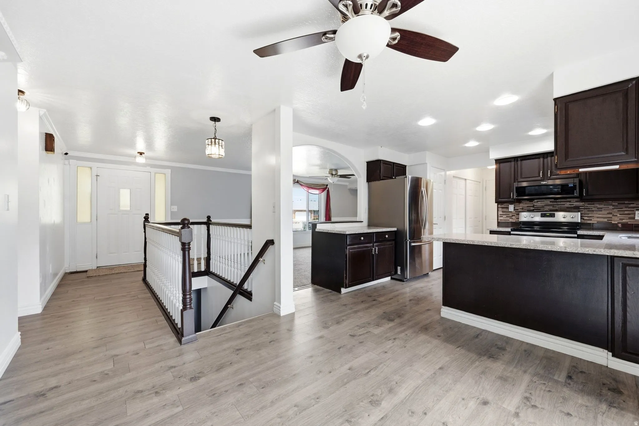 Spacious open-concept layout featuring wood-finish flooring, dark wood cabinetry, stainless steel appliances, and a central kitchen island with a light-toned countertop