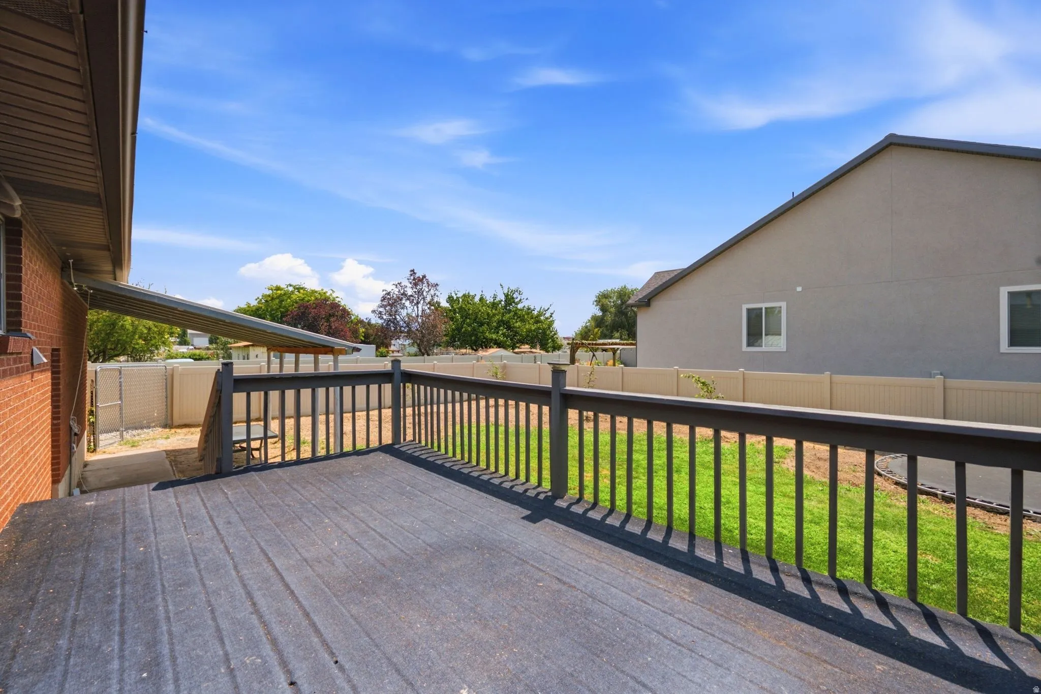 Expansive wood-finish deck with dark railing, featuring a manicured lawn and privacy fencing