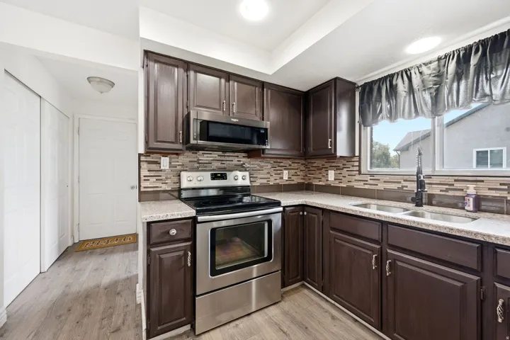Kitchen featuring wood-finish cabinetry, stainless steel appliances, a multi-tone tile backsplash, and a double basin sink