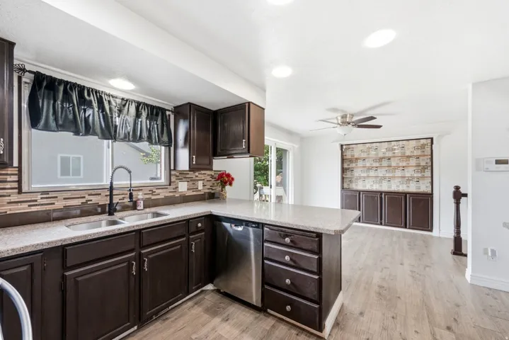 Kitchen featuring wood-finish cabinetry, light-colored countertops, stainless steel dishwasher, and a mosaic tile backsplash