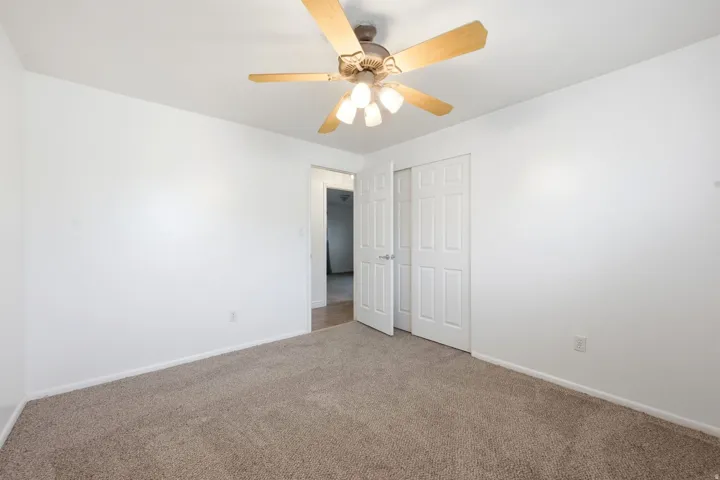 Neutral tone walls with textured carpeting, featuring a ceiling fan with integrated lighting