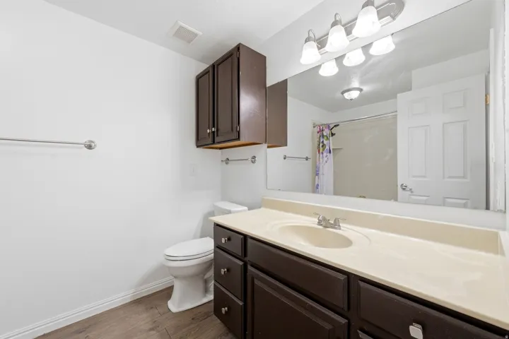 Wood-finish flooring, dark wood-finish vanity with ample storage, integrated sink, and large wall-mounted mirror