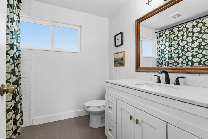 White vanity with brass hardware, undermount sink, black faucet, and a large framed mirror