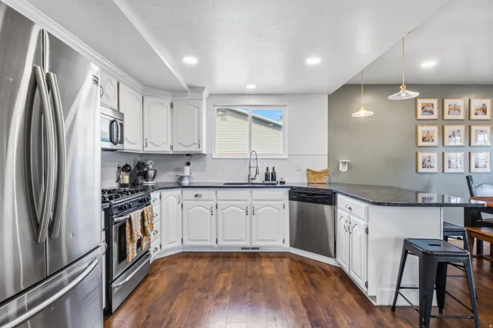 White cabinetry, dark countertops, stainless steel appliances, wood-finish flooring, and recessed lighting