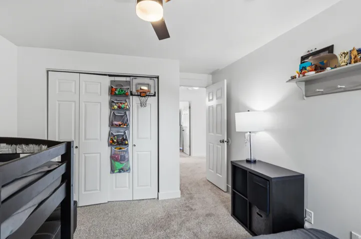 White interior walls, ceiling fan, carpet flooring, and a built-in wall shelf