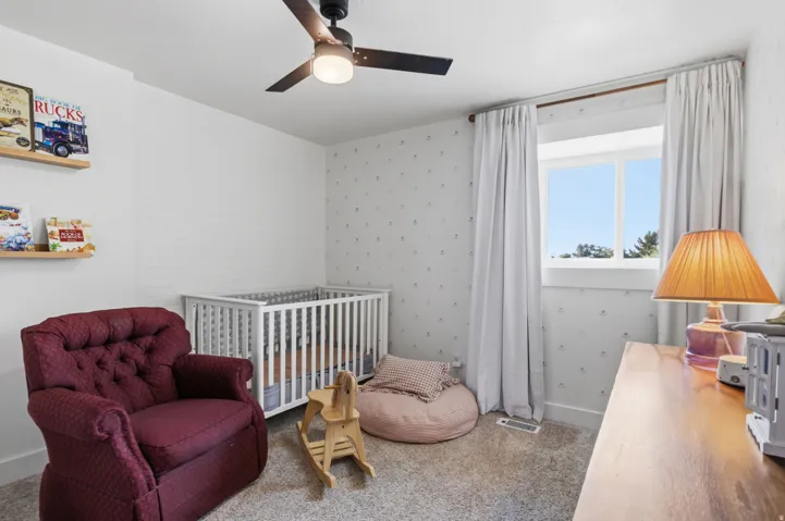 White walls with a textured accent wall, ceiling fan, and carpeted flooring
