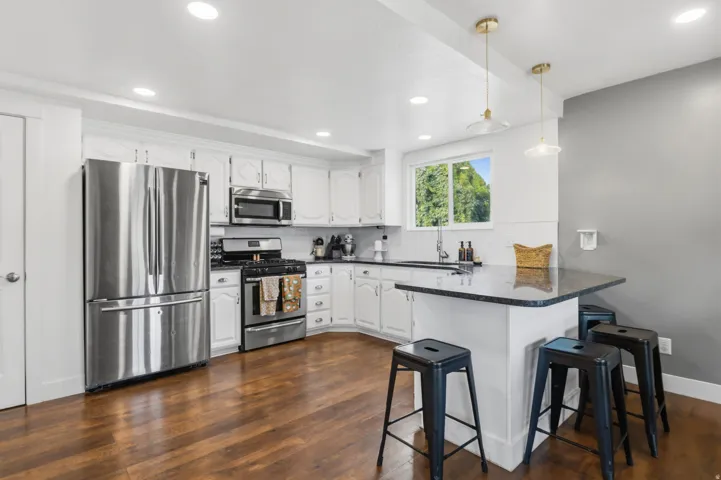 Kitchen featuring stainless steel appliances, white cabinetry, dark stone countertops, wood-finish flooring, and recessed lighting