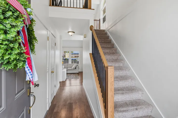 Entryway featuring wood-finish flooring, a carpeted staircase with wood and metal railing, and a vaulted ceiling