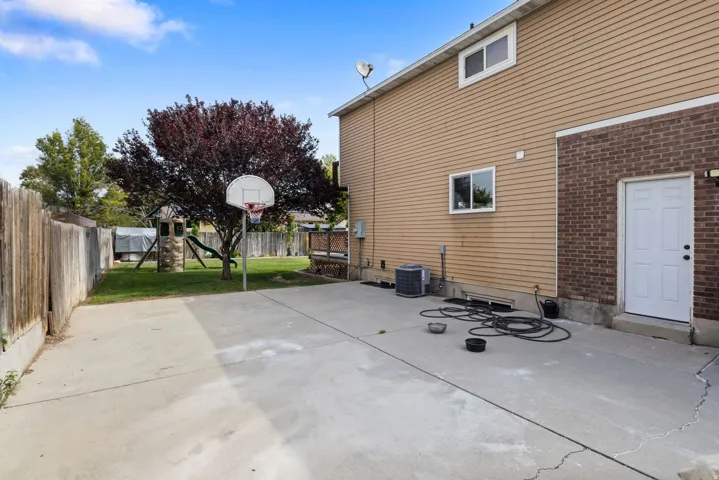 Expansive concrete patio with a basketball hoop, leading to a lawn area with a mature tree