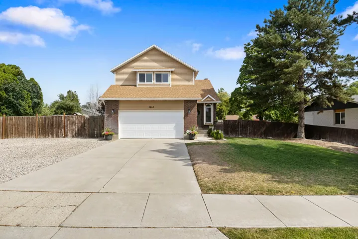 Two-story residence featuring brick and siding facade, an attached garage, paved driveway, and a front lawn with mature trees