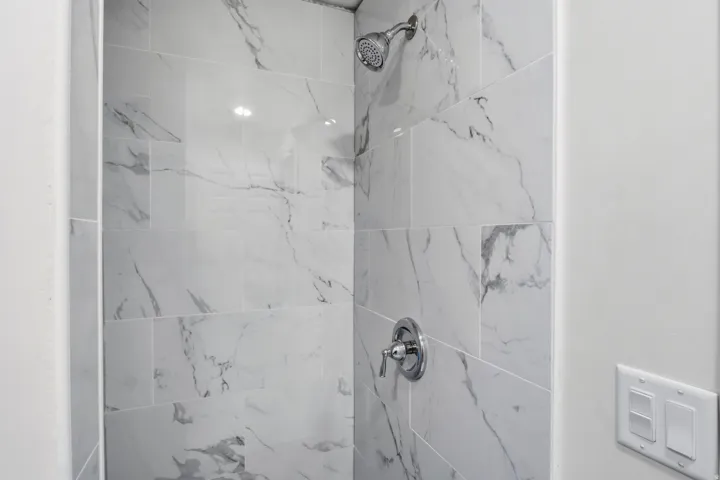 Shower with large format marble-look tile, chrome fixtures, and recessed lighting