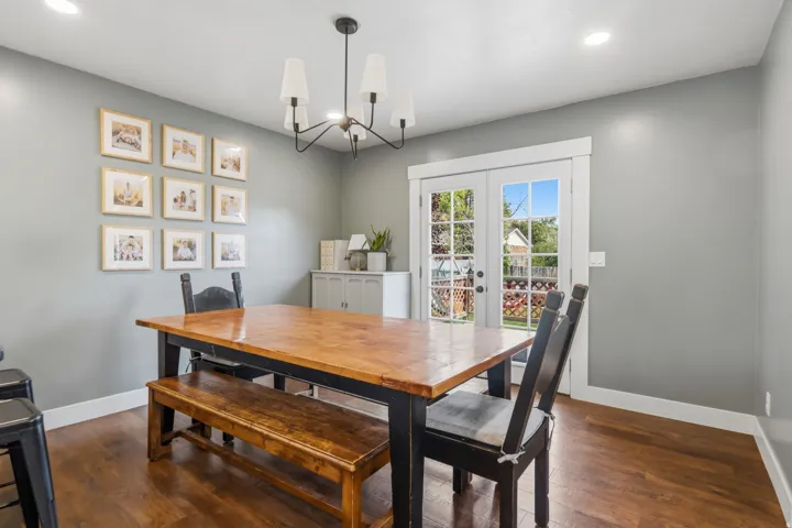 Hardwood flooring, recessed lighting, and a modern chandelier illuminate this space, featuring a built-in cabinet and French doors