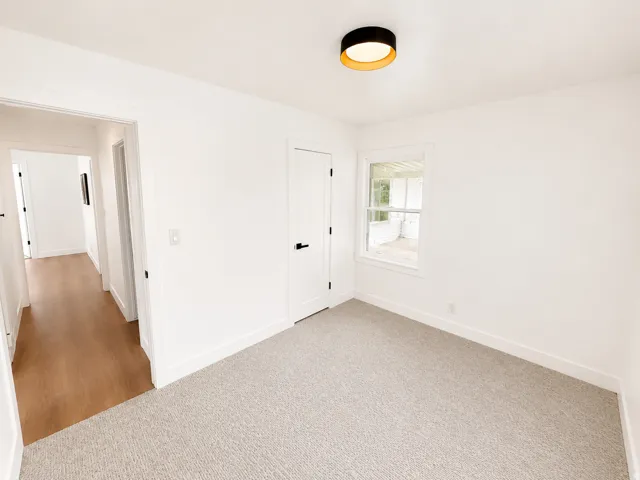 Recessed window with white trim, light gray carpet flooring, white walls, and a modern flush-mount ceiling light