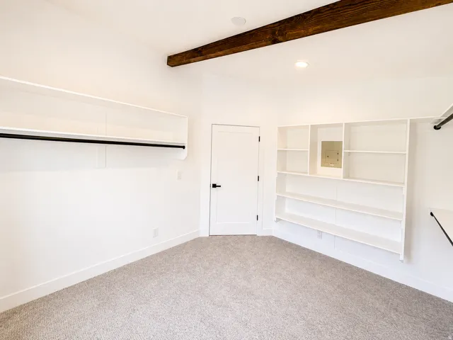 Exposed wood beam ceiling, recessed lighting, built-in shelving, white door with matte black hardware, and gray carpet flooring
